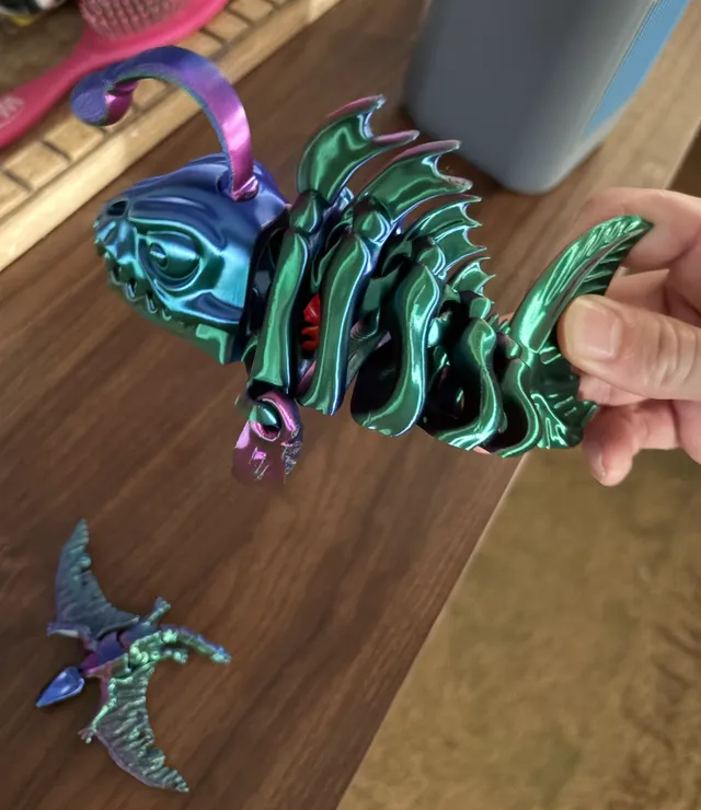 Articulated skeleton angler fish 3D print held in a hand, showing green and blue color-shift filament