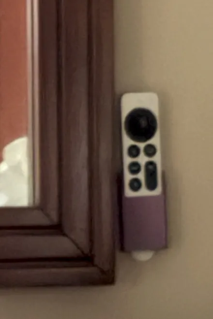Purple 3D printed wall holder mounted beside a mirror, cradling an Apple TV remote
