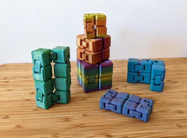 Stack of colorful 3D printed infinity cube fidgets on a wooden table