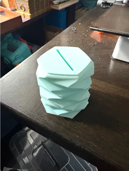 Mint green 3D printed piggy bank with a twisted, faceted geometric shape and a coin slot on top