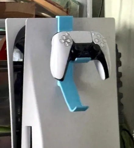 Light blue 3D printed wall mount hooked over the edge of a PS5 console, holding a white DualSense controller