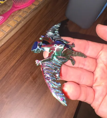 Small articulated pterodactyl 3D print with spread wings resting in an open hand, printed in iridescent color-shift filament